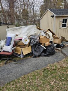 A large pile of boxes, bags, a chair, and a mattress outside a shed, ready for junk removal by Rizzo Junk Removal in Nashua, NH.