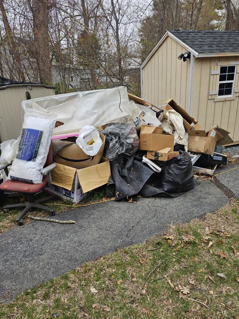 A large pile of boxes, bags, a chair, and a mattress outside a shed, ready for junk removal by Rizzo Junk Removal in Nashua, NH.