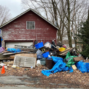 A large pile of various junk and debris outside a red shed, ready for removal by Avery's Junk Removal & Hauling in Trenton, MI.