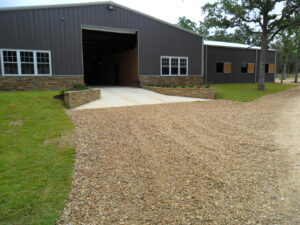 A large metal building with stone accents and a gravel driveway, showcasing a completed project by Austin Roofing and Construction in Austin, TX.