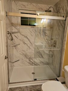 A large, modern shower installation with marble-look panels and a glass door by Peninsula Bath & Tile in Salisbury, MD.
