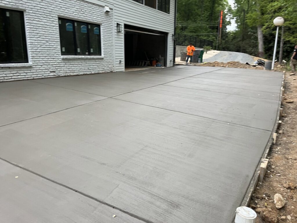 A large, newly poured concrete driveway or slab next to a residential garage by Rodriguez Concrete Creations in Rock Hill, SC.