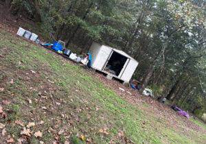 A wide view of a large outdoor junk pile and a shed in a wooded area, indicating a significant cleanout by Junk Hawgs Removal and Rentals in Russellville, AR.