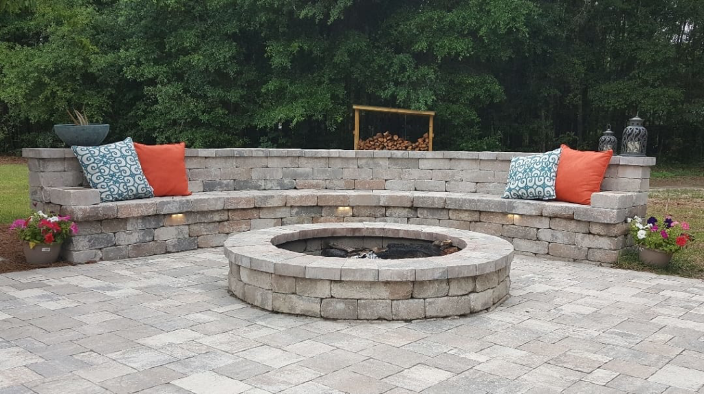 A large paver patio featuring a circular fire pit and curved seating wall with lighting by Keystone Design in Tallahassee, FL.