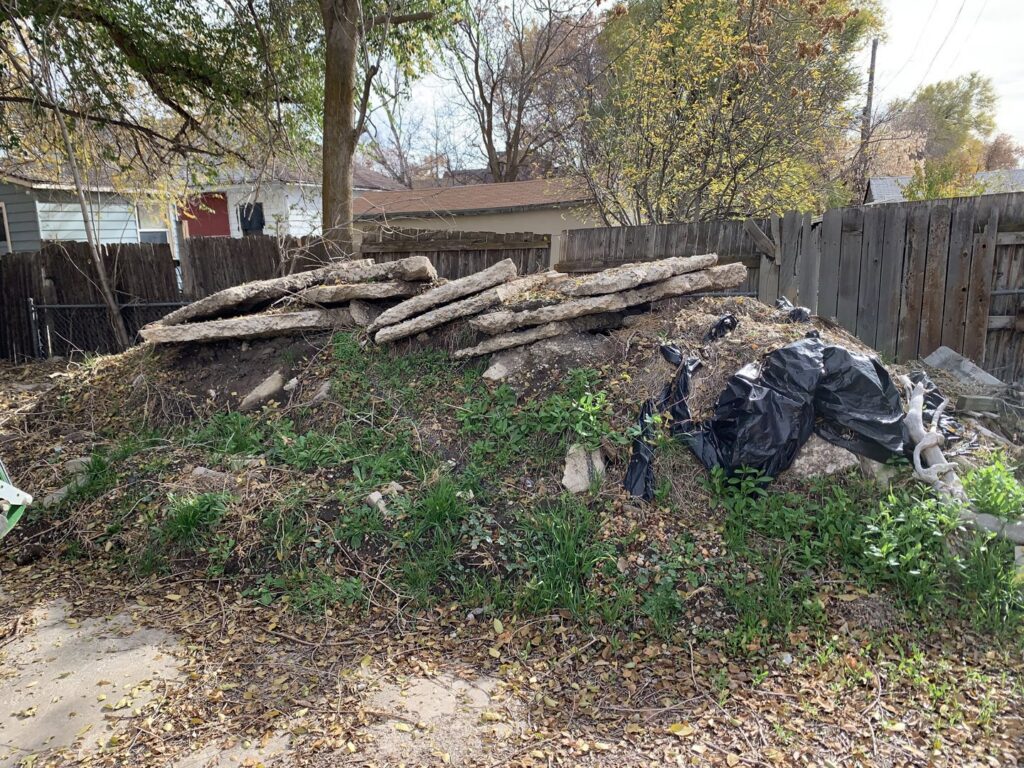 A large pile of concrete slabs and dirt in a backyard, indicating a debris removal job for Junk Solutions in Ogden, UT.