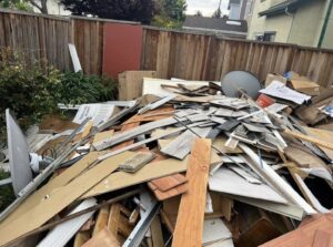 A large pile of mixed construction debris and household junk in a backyard, ready for removal by Stars Junk Removal in San Jose, CA.