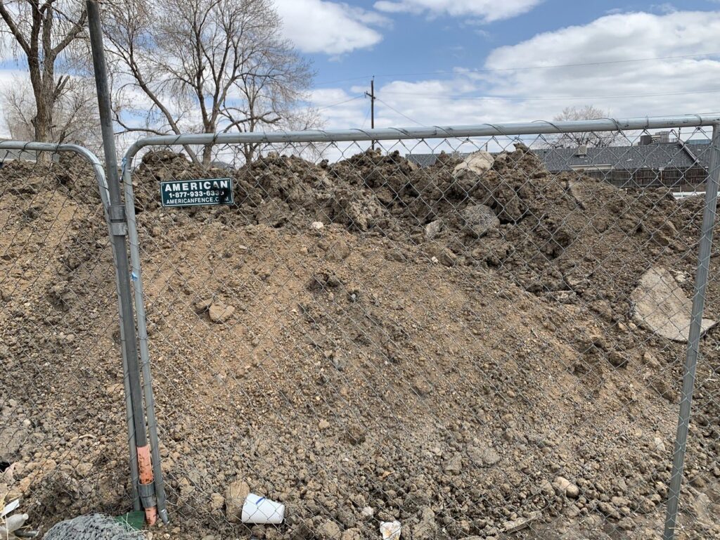A large pile of dirt and debris behind a chain-link fence, indicating a site cleanup or junk removal project by Discount Dumpster in Naples, FL.
