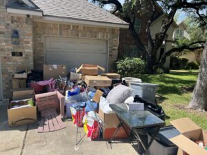 A large pile of household junk, including boxes, chairs, and bags, in a driveway for removal by SATX Junk-A-Haulics in San Antonio, TX.