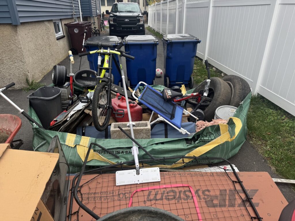 A large pile of household junk and debris in a side yard, ready for removal by Altri Junk Removal Services in Lynn, MA.