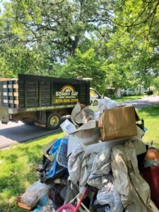 A large pile of household junk and debris on a lawn with a Sonny Day Junk Removal truck in the background in Batesville, AR.