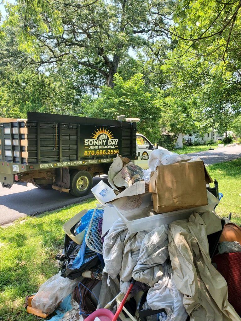 A large pile of household junk and debris on a lawn with a Sonny Day Junk Removal truck in the background in Batesville, AR.