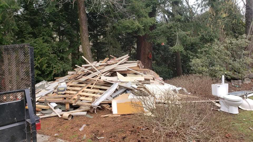 A large pile of construction debris, wood, and old toilets in a yard, ready for removal by Junk Management in Vancouver, WA.
