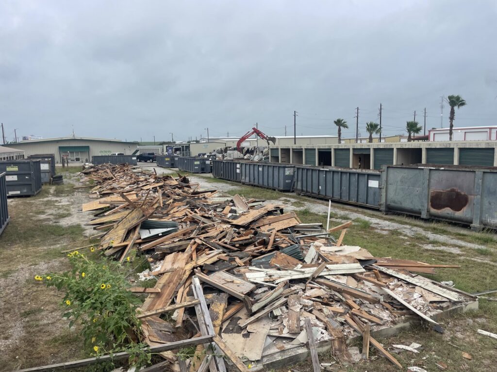 A large pile of wood and mixed demolition debris with dumpsters and an excavator in the background from White Star Services LLC in Corpus Christi, TX.