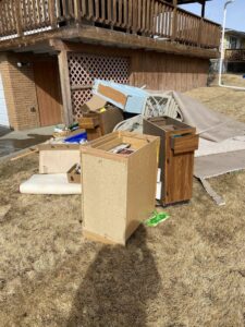 A large pile of old furniture, wood, and construction debris outside a residential home, ready for removal by Hudson's Trash Removal, LLC in Great Falls, MT.