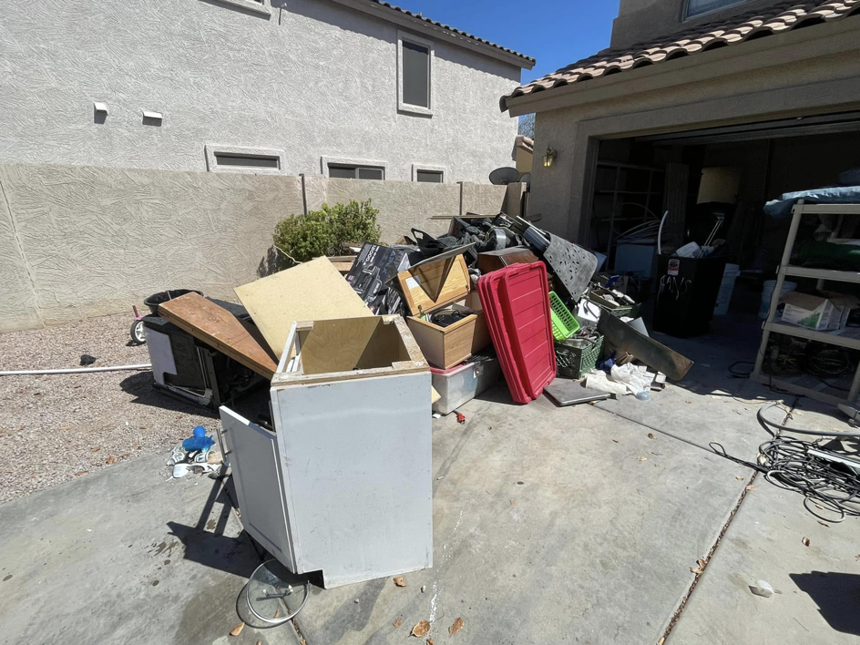 A large pile of household junk and debris ready for removal outside a garage by Canyon State Junk Removal in Peoria, AZ