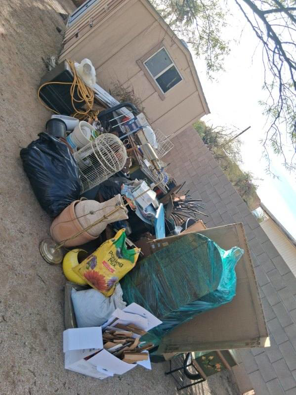 A large pile of various household junk and debris, including furniture and bags, stacked next to a shed for removal by Vista Clean Junk Removal in Tucson, AZ.