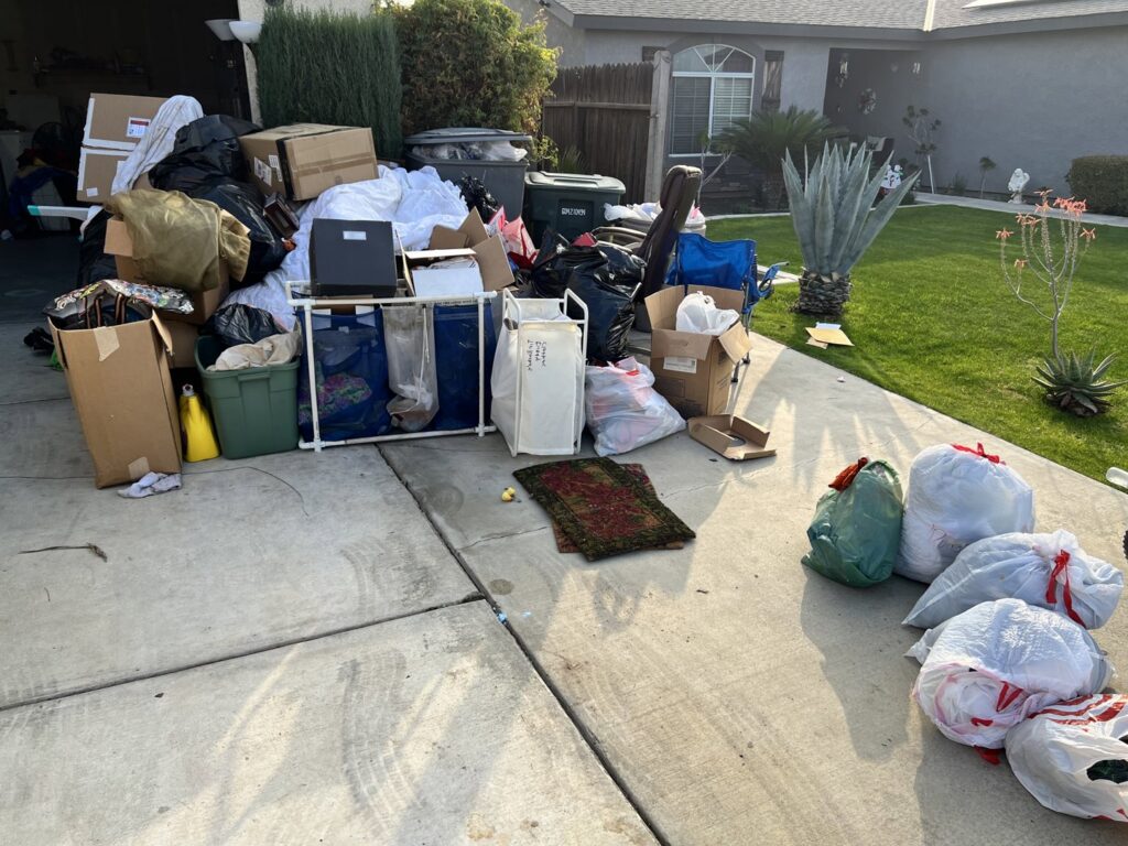 A large pile of household junk, including boxes and trash bags, awaiting removal on a residential driveway in Bakersfield, CA.