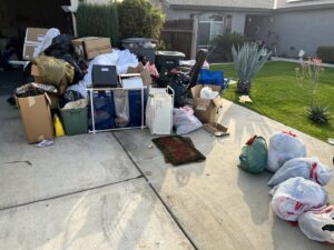 A large pile of household junk, including boxes and trash bags, awaiting removal on a residential driveway in Bakersfield, CA.