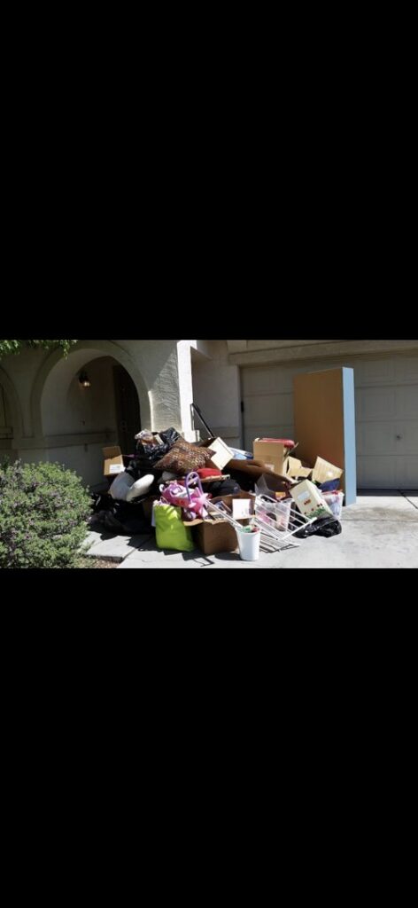 A large pile of mixed household junk, including boxes and various items, placed outside a garage for removal by The Junkporter Junk Removal in Las Vegas, NV.