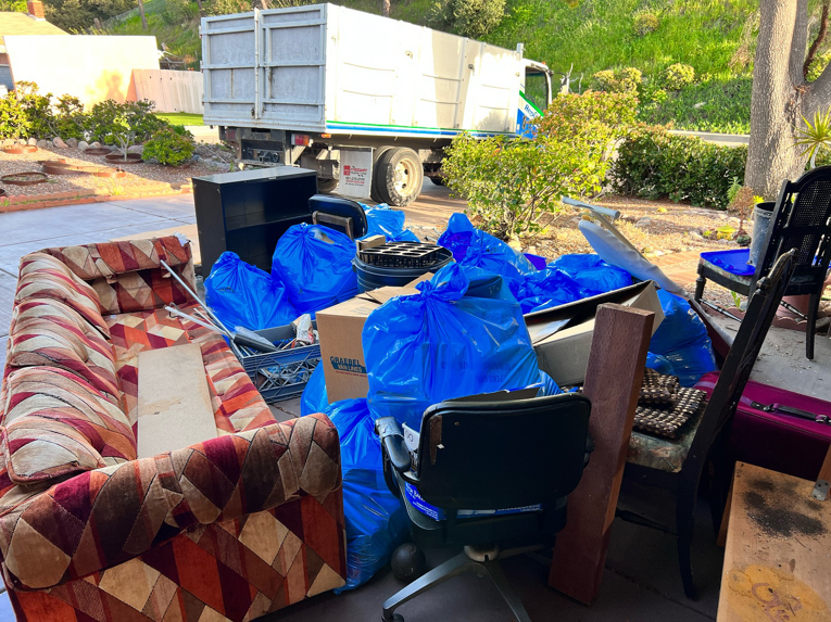 A large pile of household junk, including a sofa and bagged items, ready for Republic Junk Removal in San Diego, CA.