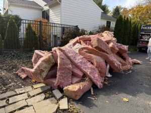 A large pile of pink insulation debris on a driveway, ready for general junk removal by Anywhere Dumpster Rental in Naperville, IL.