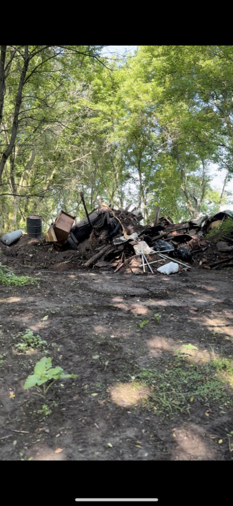 A large, unsightly pile of various junk and scrap metal in a wooded area, indicating a site ready for cleanup by Speedy Scrap Junk Removal LLC in Portage, WI.