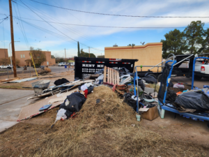 A large pile of mixed junk and debris next to a Highland Dumpster Rentals LLC dumpster in Las Cruces, NM.