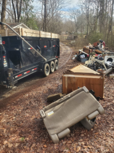 A large pile of household junk and debris next to a dumpster trailer, awaiting removal by Standard Dumpster LLC in Rock Hill, SC.