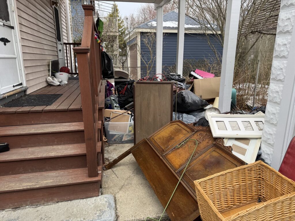 A large pile of old furniture, bags, and boxes on a residential porch, awaiting junk removal by The Junkluggers in Hicksville, NY.