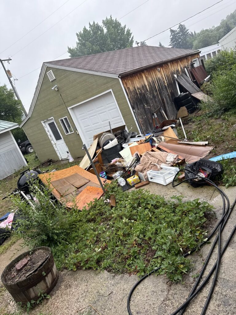 A large pile of assorted junk and debris outside a garage, ready for removal by Hudson's Trash Removal, LLC in Great Falls, MT.
