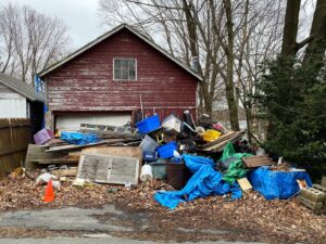 A large pile of various junk, including tarps, wood, and plastic bins, accumulated outside a garage, ready for junk removal in Sterling Heights, MI.