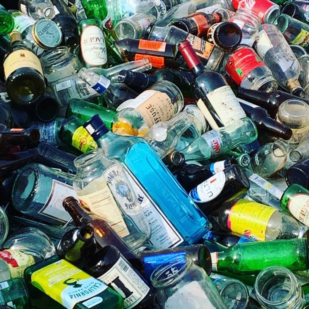 A large pile of mixed glass bottles and jars, representing materials collected for recycling by Fisher Recycling in Charleston, SC.