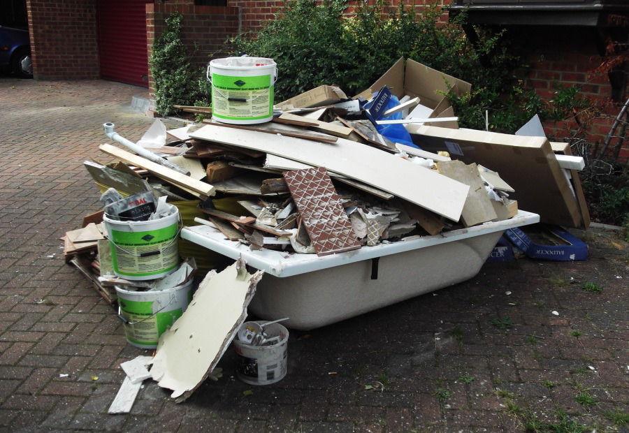 A large pile of mixed junk and construction debris, including a broken bathtub and wood, on a paved driveway for DFW Service People in Dallas, TX.