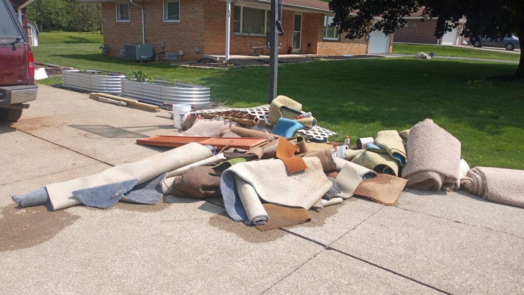 A large pile of old rolled carpets and construction debris on a driveway, ready for HAULA Junk Removal in Canton, OH.