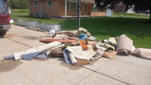 A large pile of old rolled carpets and construction debris on a driveway, ready for HAULA Junk Removal in Canton, OH.
