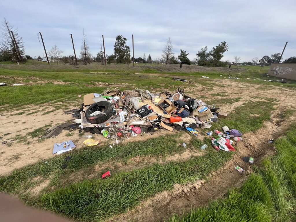 A large pile of trash and debris in a grassy field, indicating a junk removal job for Sac Junk in Rancho Cordova, CA