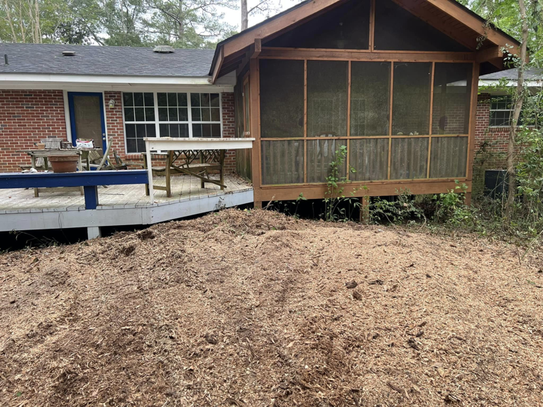 A large pile of fresh wood chips next to a residential deck, showing the result of stump grinding by Manley's Stump Grinding in Opelika, AL.
