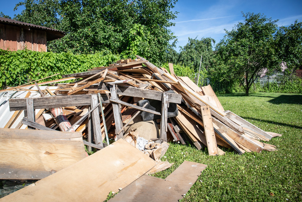 A large pile of wood and construction debris in a grassy yard, indicating a need for junk removal services by Dumpster 360 in Clarksville, TN.