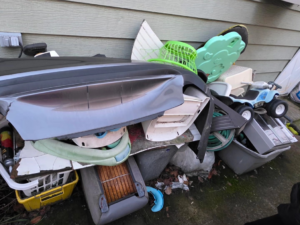 A large pile of yard and household junk stacked against a house, ready for Squirrel Squad LLC in Portland, OR.