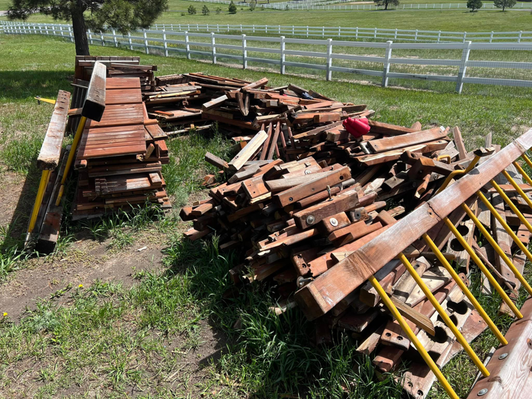 A large pile of wooden debris and old lumber in a grassy yard, ready for removal by Mile High Junk in Aurora, CO.