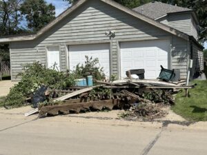 A large pile of yard waste and mixed debris in front of a residential garage, ready for removal by Siouxland Junk Removal in Sioux City, IA.