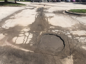 A large pothole filled with water in an asphalt parking lot, ready for repair by Gorman sealcoating & striping in Blue Springs, MO.