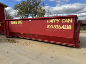 A large red dumpster from Happy Can Disposal parked on a concrete surface, available for junk removal in Flint, MI.