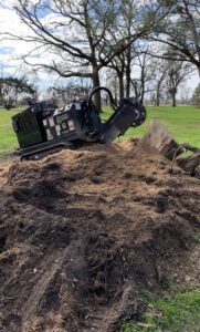 A stump grinder machine next to a large pile of wood chips and dirt from a recent stump removal by Stumps Be Gone in Augusta, GA.