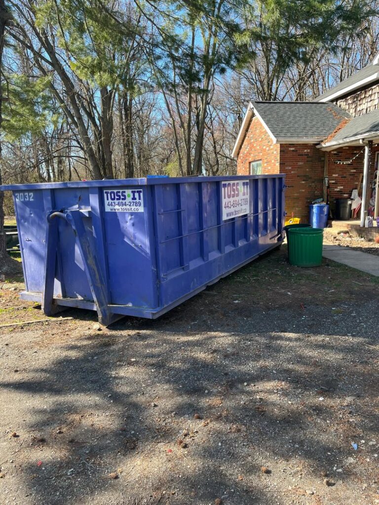 A large blue Toss-It roll-off dumpster placed in a residential driveway for junk removal in Baltimore, MD.