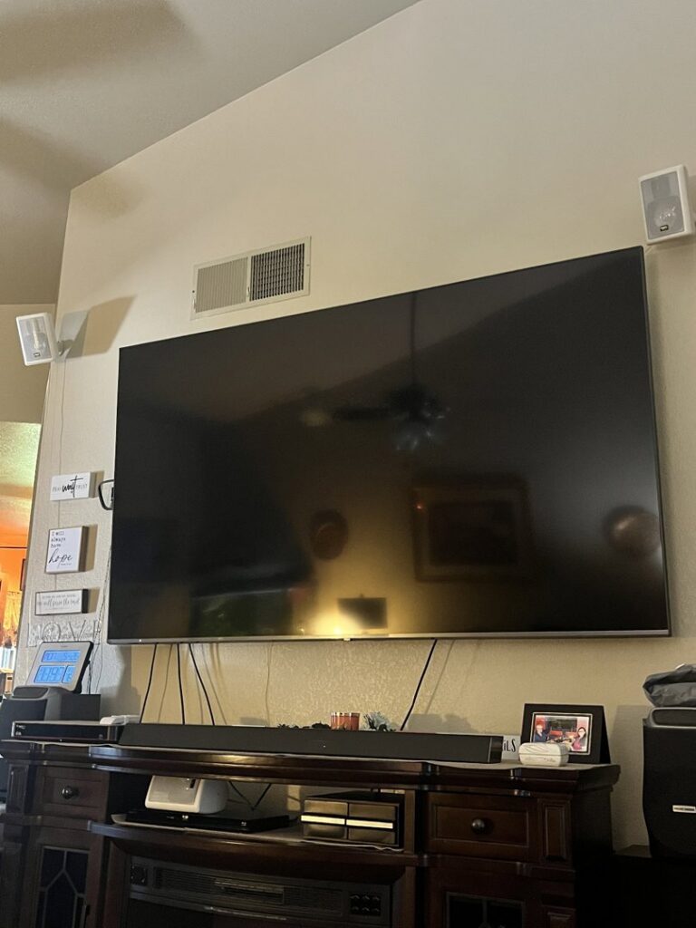 A large TV and two white speakers professionally mounted on a wall, showcasing installation by Tech Handy-Las Vegas in North Las Vegas, NV.