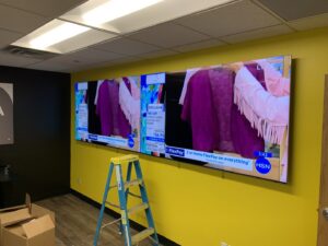 A large television being mounted on a yellow wall, a commercial service by I Know A Guy Handyman Service, Cottage Grove, MN.