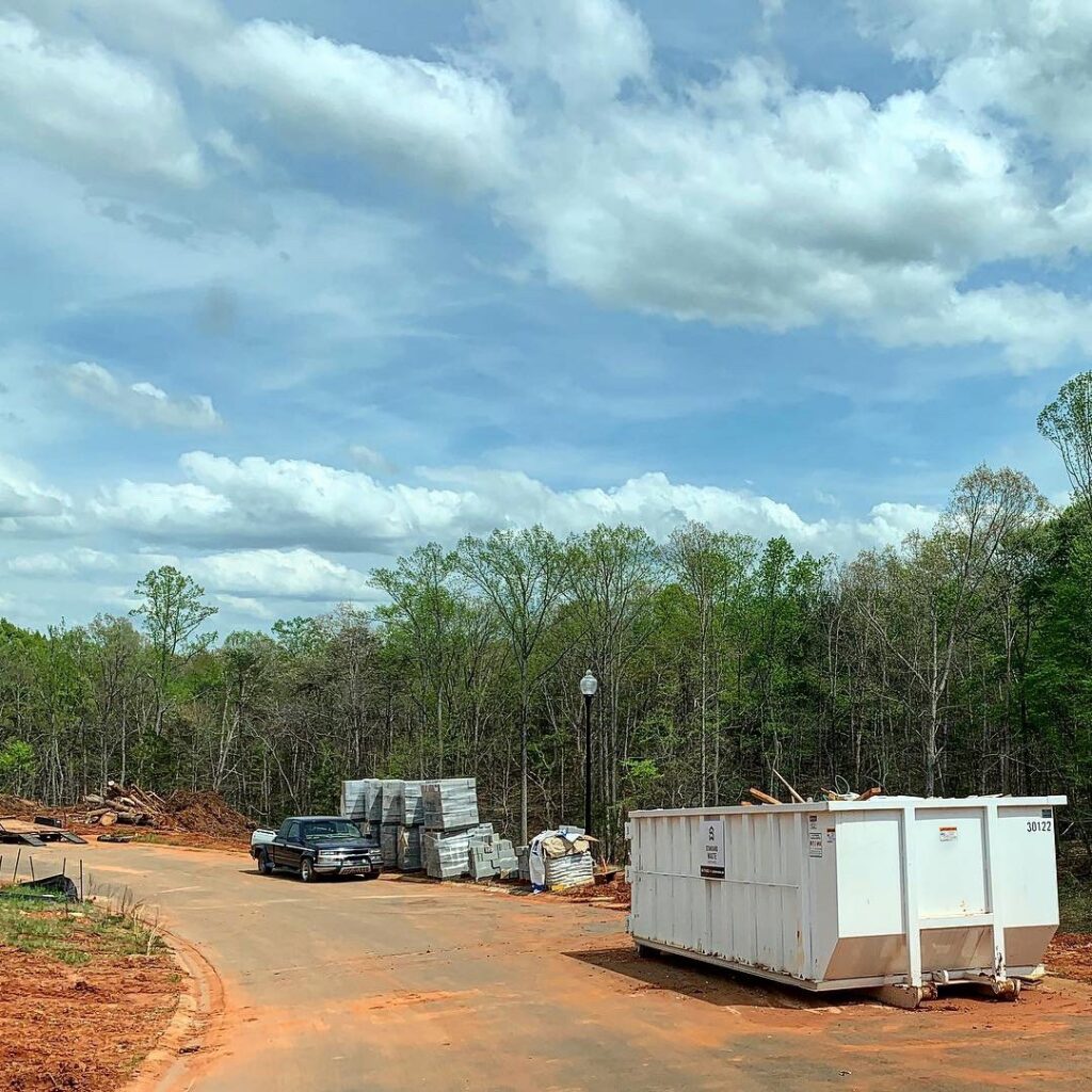 A large white dumpster at a construction site with building materials, ready for junk removal by Standard Waste Enterprises in Greenville, SC.