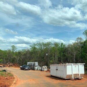 A large white dumpster at a construction site with building materials, ready for junk removal by Standard Waste Enterprises in Greenville, SC.