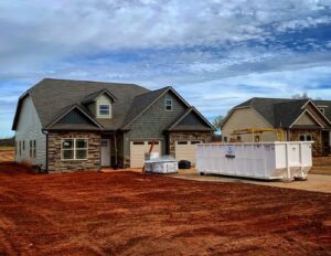 A large white dumpster placed in front of a newly built house at a construction site, for junk removal by Standard Waste Enterprises in Greenville, SC.